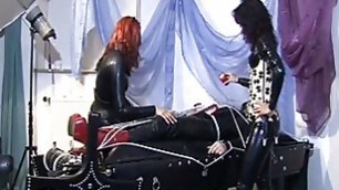 Two naughty dominas in latex tie up a slaves cock and torture it